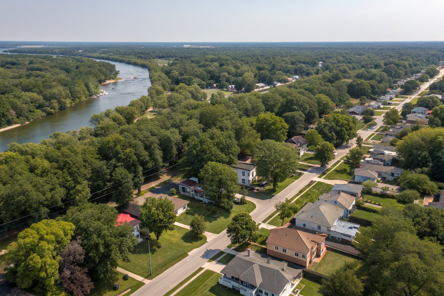 Aerial view of tree-lined streets of older houses beside a wide, slow river